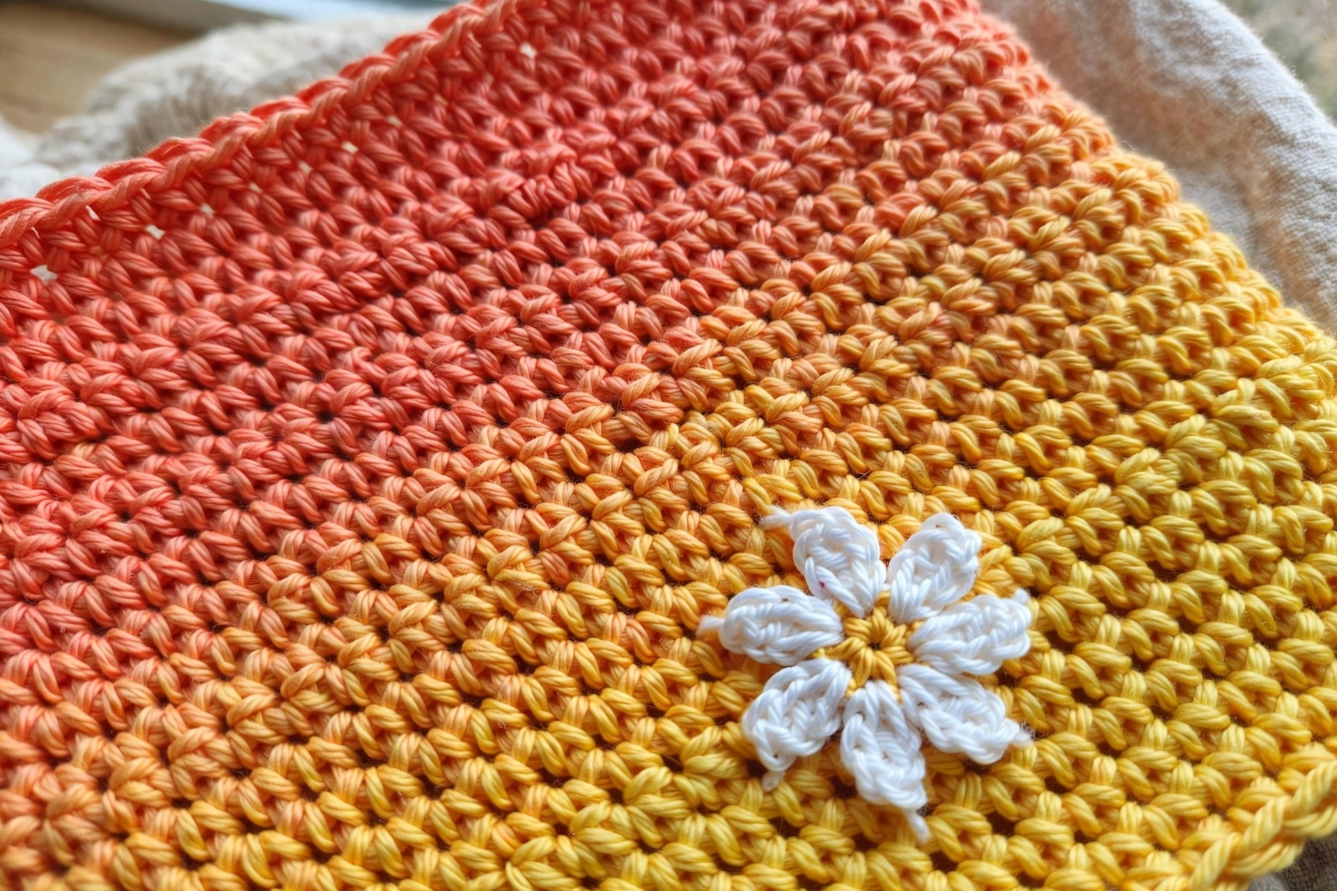 Close-up of the coral-to-yellow ombre single crochet fabric with daisy applique