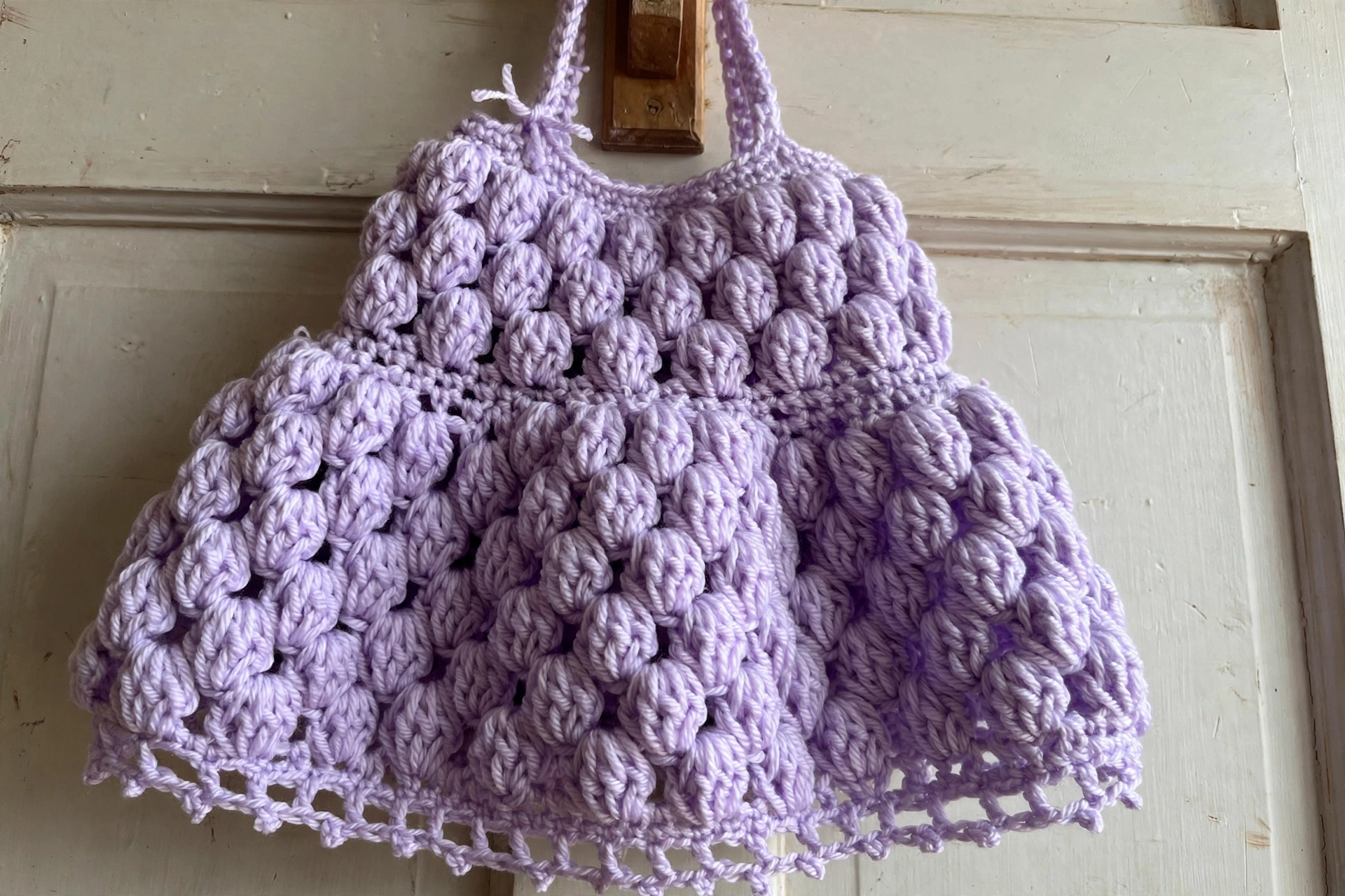 Close-up of the bubbly lavender puff-stitch texture with picot hem of the baby dress