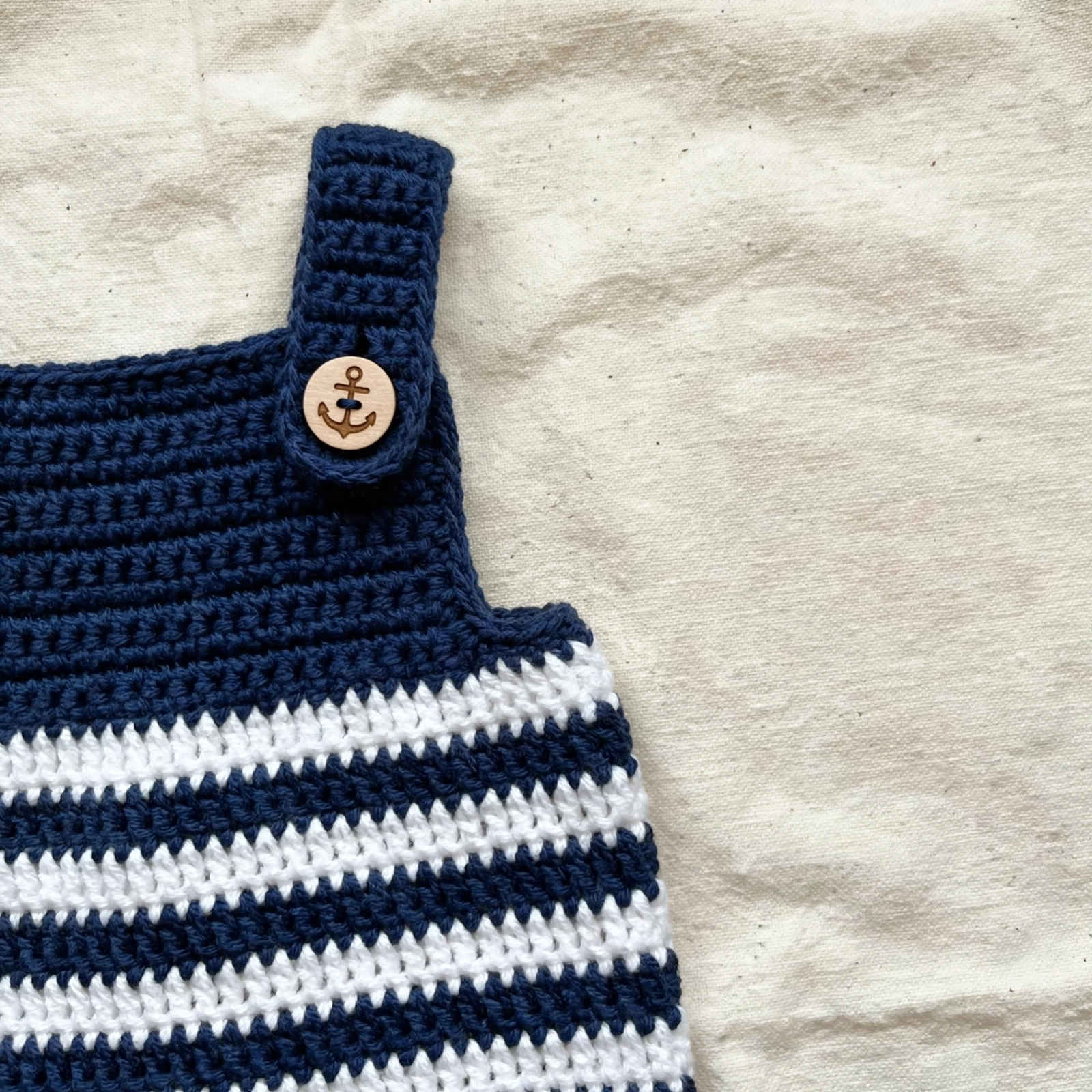 Close-up of the navy and white striped crochet overalls with an anchor-engraved wooden button