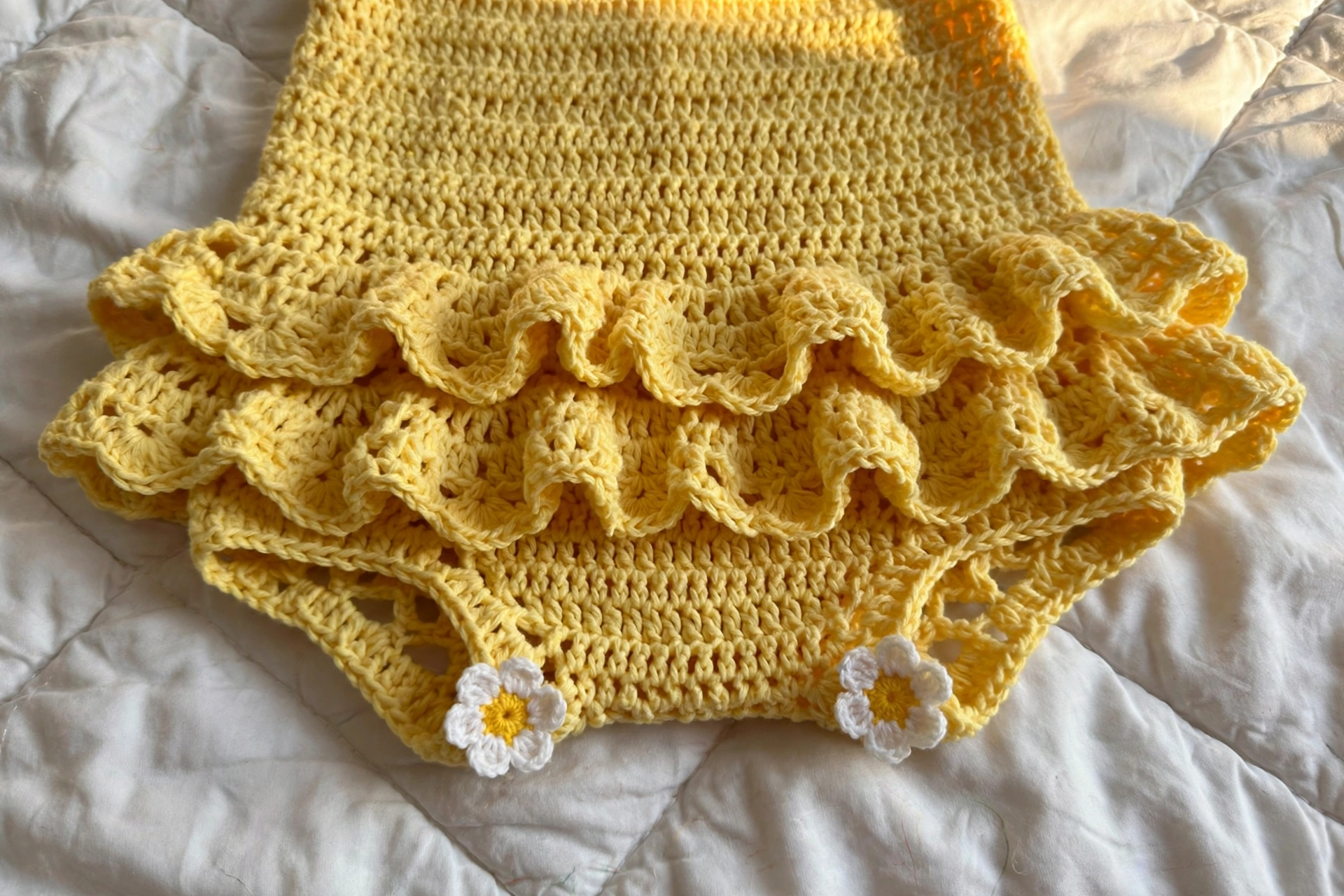 Close-up of double ruffle tiers and daisy appliques on the yellow baby romper